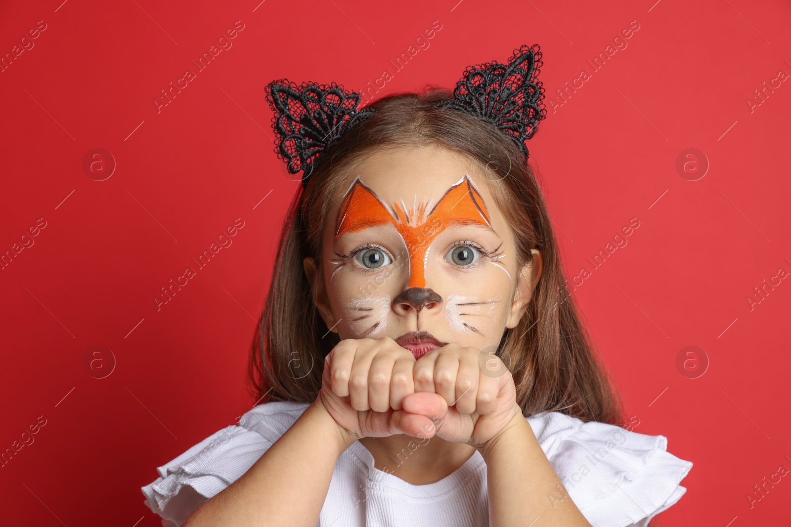 Photo of Cute girl with painted face and ears as cat on red background