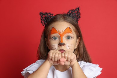 Cute girl with painted face and ears as cat on red background