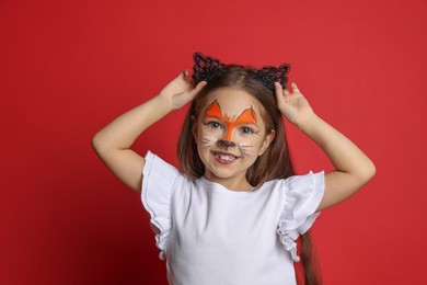 Photo of Cute girl with painted face and ears as cat on red background