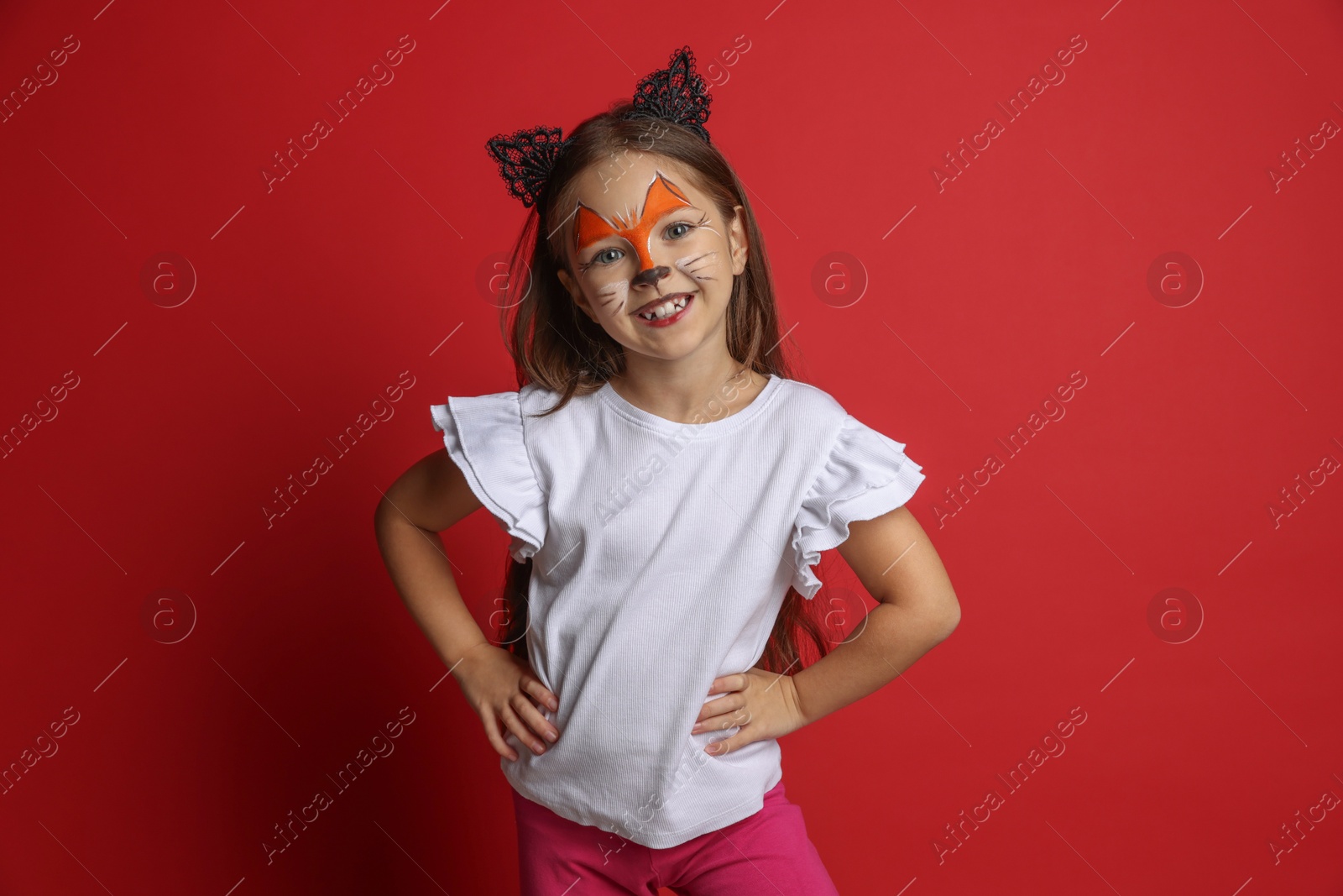 Photo of Cute girl with painted face and ears as cat on red background