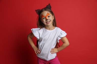 Photo of Cute girl with painted face and ears as cat on red background