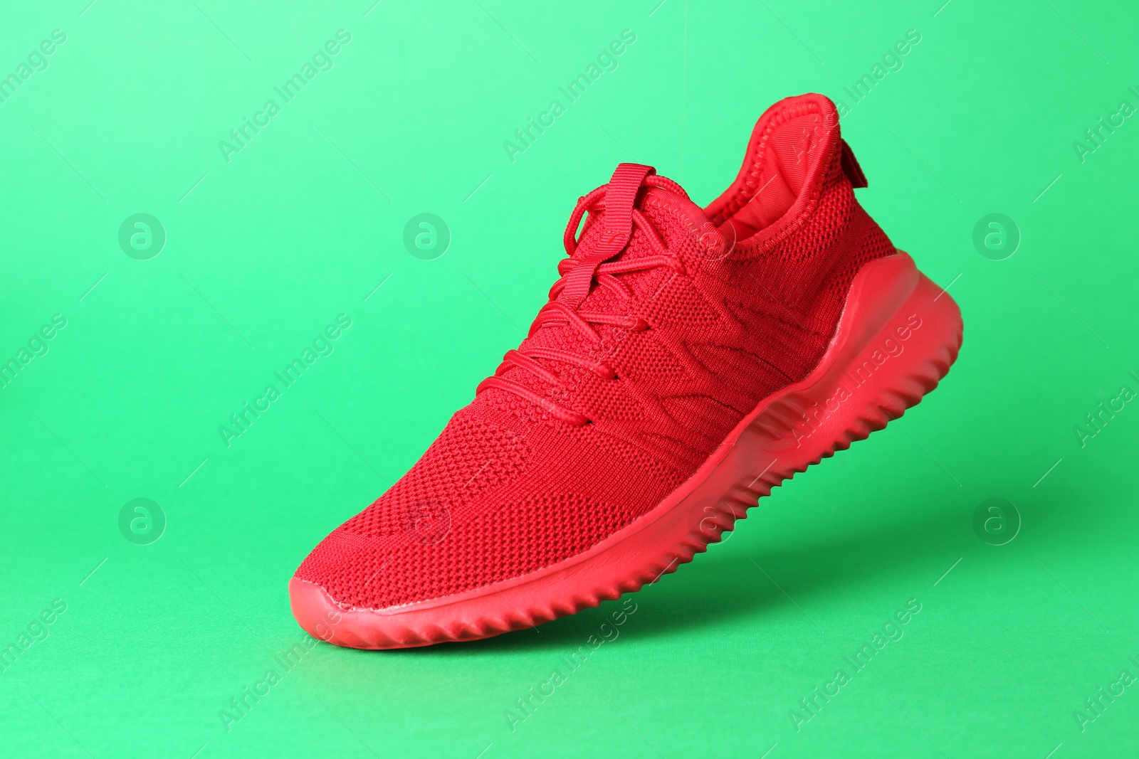 Photo of Stylish red sneaker in air against green background