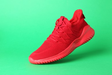 Photo of Stylish red sneaker in air against green background