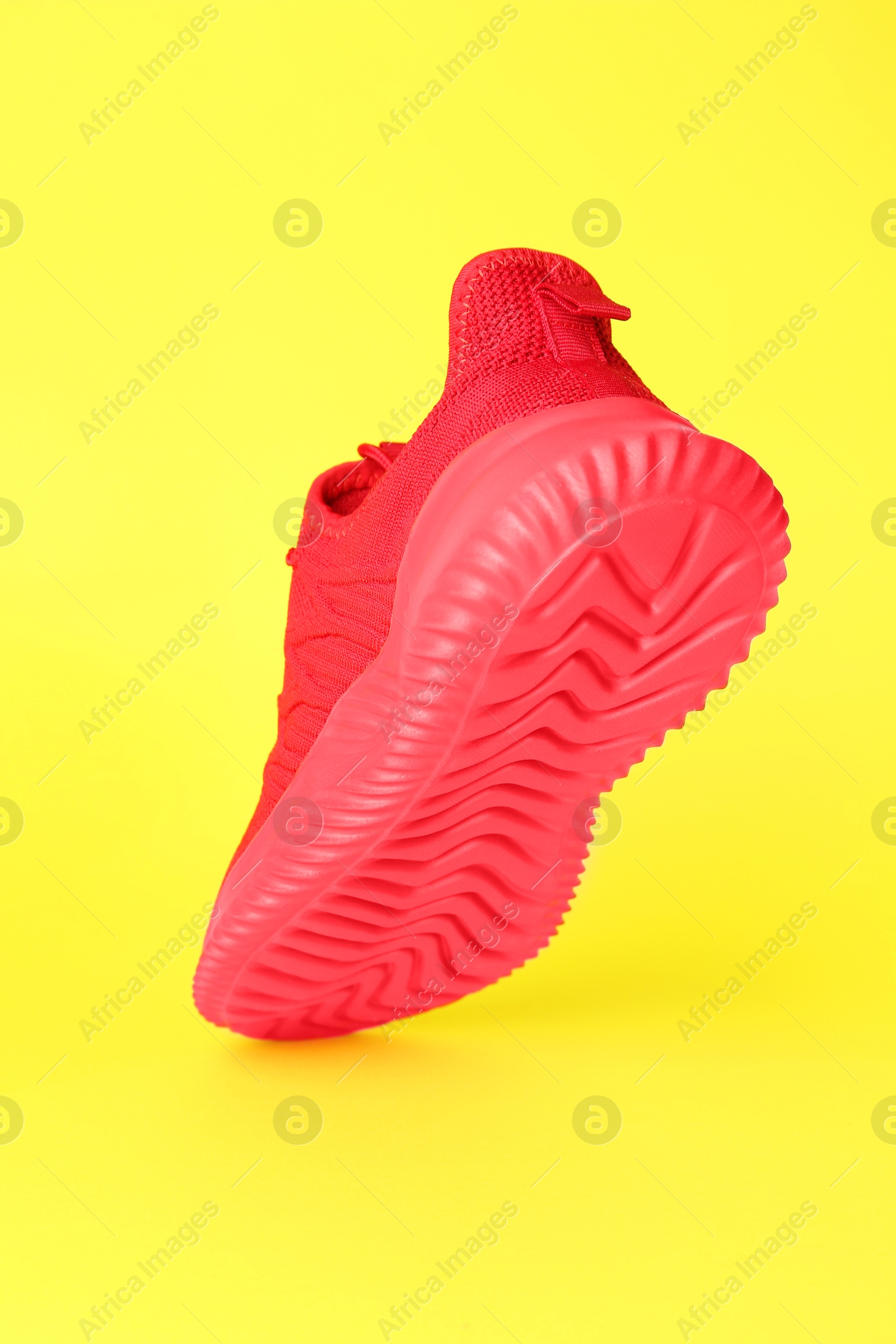 Photo of Stylish red sneaker in air against yellow background