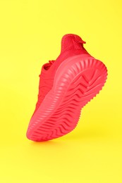 Photo of Stylish red sneaker in air against yellow background