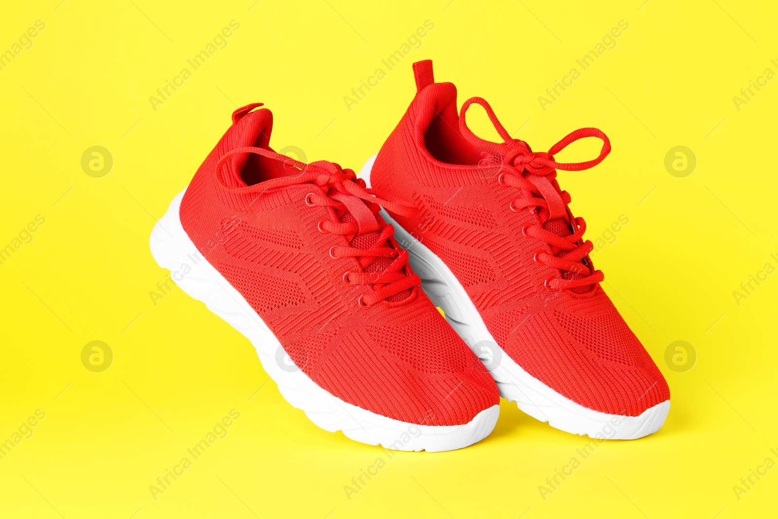 Photo of Pair of stylish red sneakers in air against yellow background