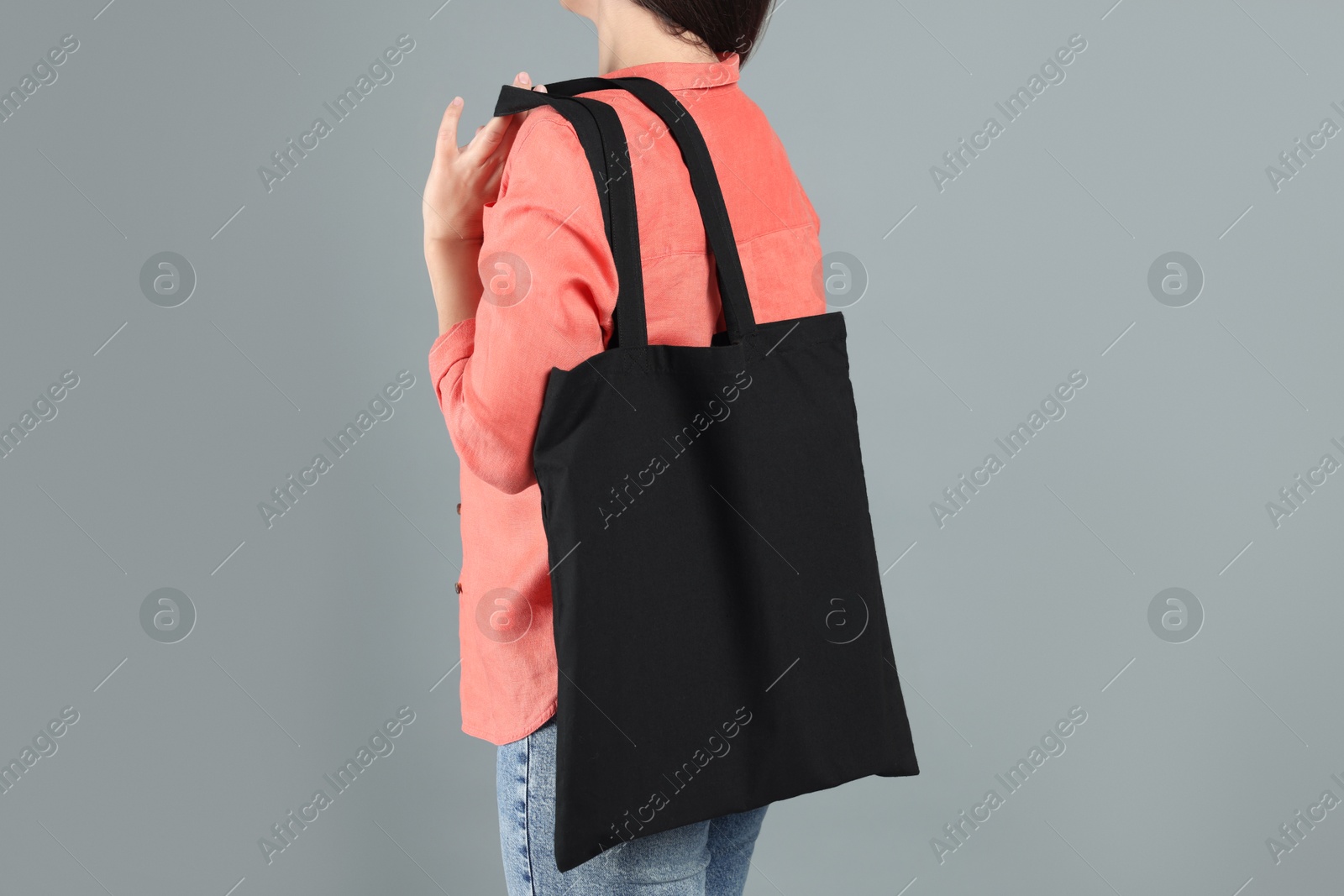 Photo of Woman with blank black shopper bag on grey background, back view. Mockup for design