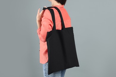 Woman with blank black shopper bag on grey background, back view. Mockup for design