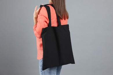 Woman with blank black shopper bag on grey background, back view. Mockup for design