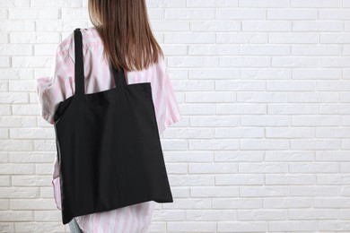 Woman with blank black shopper bag near white brick wall, back view. Mockup for design