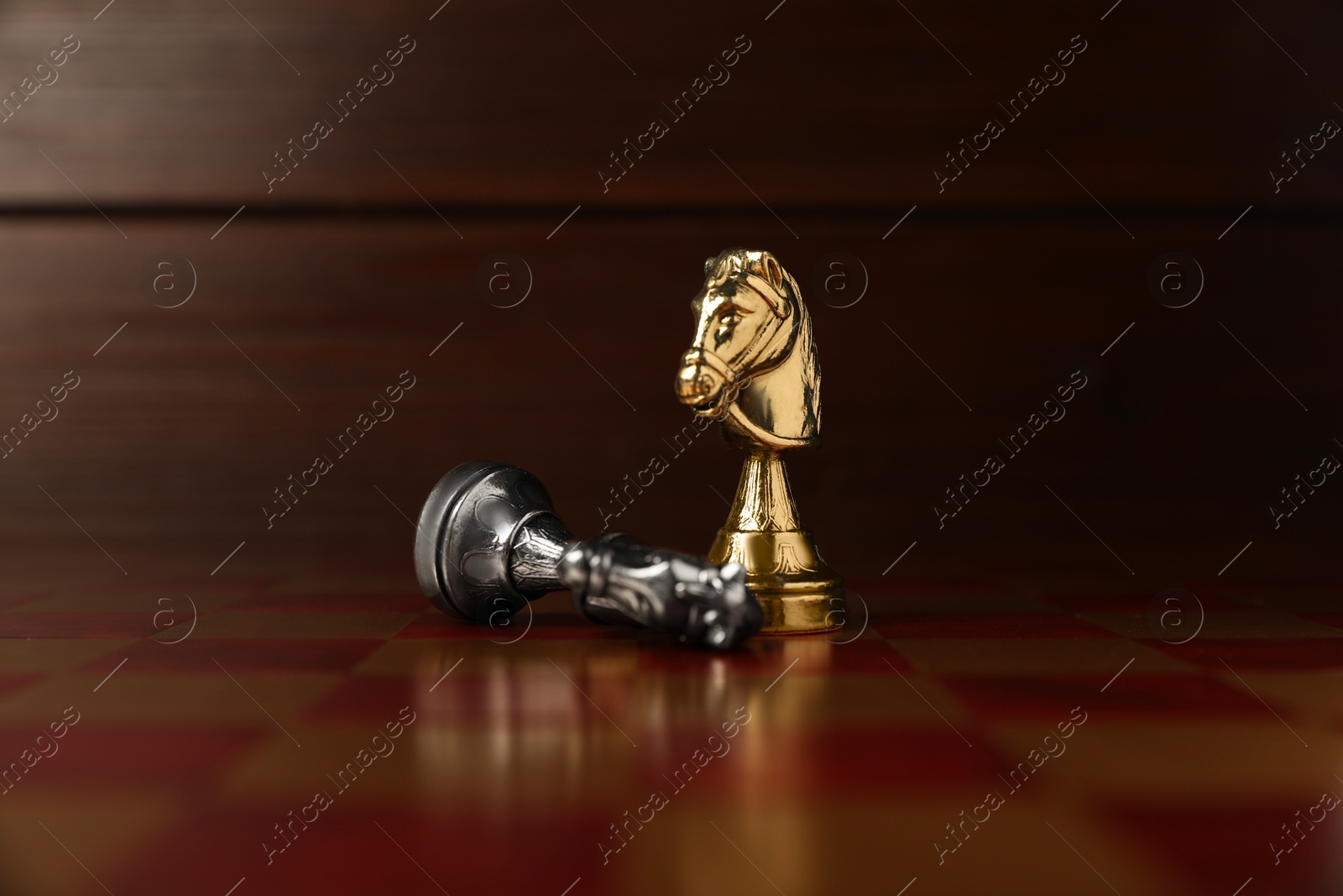 Photo of Golden chess knight near fallen silver one on chessboard. Competition concept