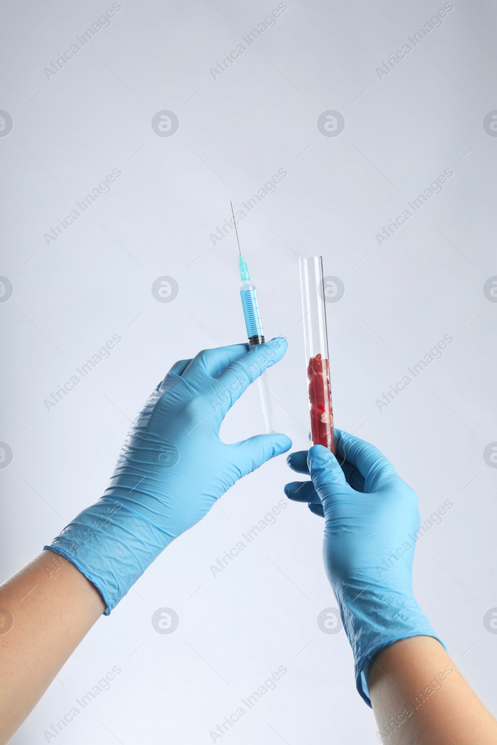 Photo of GMO concept. Scientist with syringe and piece of meat in test tube on white background, closeup