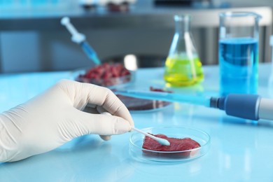 Photo of GMO concept. Scientist with swab and piece of meat at table in laboratory, closeup