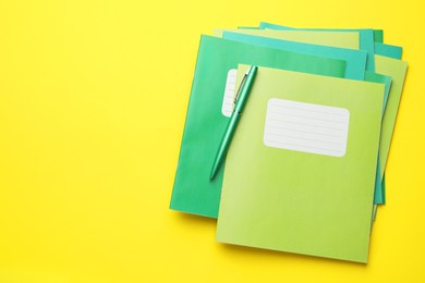 Photo of Stack of copybooks and pen on yellow background, top view. Space for text