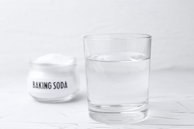 Photo of Glass of water and baking soda on white textured table, selective focus