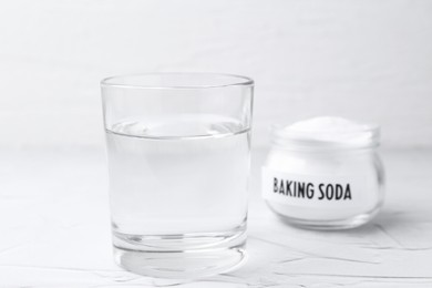 Photo of Glass of water and baking soda on white textured table, selective focus