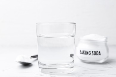 Photo of Glass of water and baking soda on white textured table, selective focus