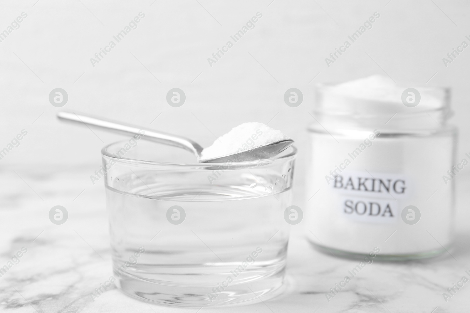 Photo of Glass of water and baking soda on white marble table, selective focus