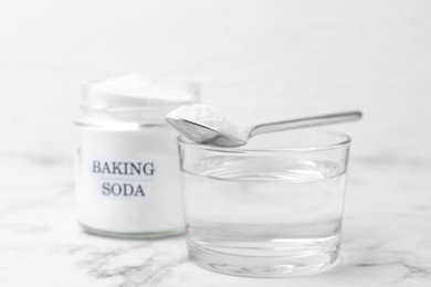 Photo of Glass of water and baking soda on white marble table, selective focus