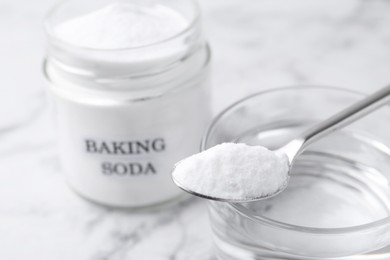 Photo of Glass of water and baking soda on white marble table, selective focus