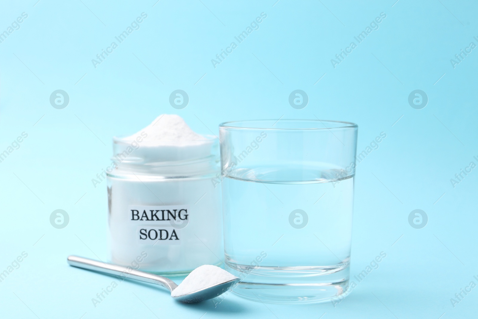 Photo of Glass of water and baking soda on light blue background