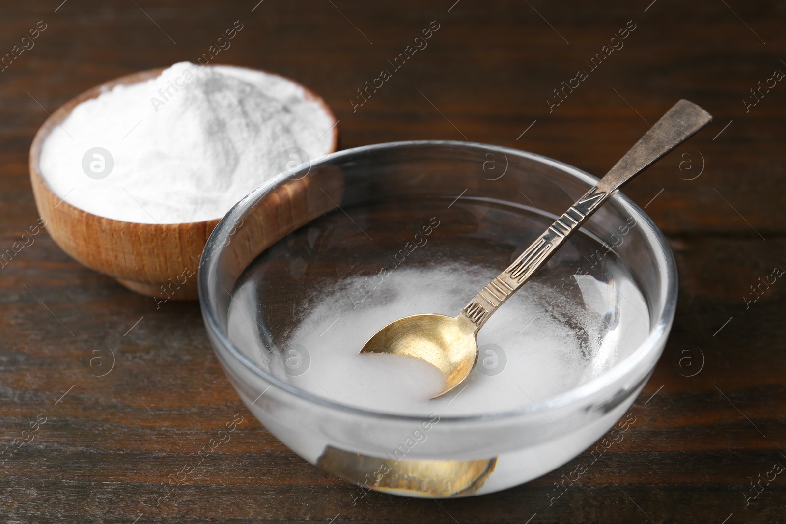 Photo of Bowl with water and baking soda on wooden table, closeup