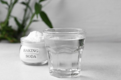 Photo of Glass of water and baking soda on white table, selective focus