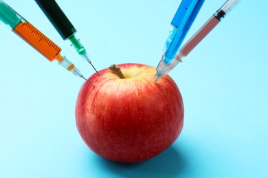 Photo of GMO concept. Red apple with different syringes on light blue background, closeup