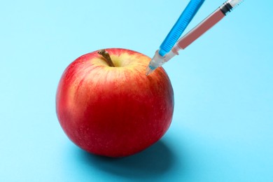 Photo of GMO concept. Red apple with different syringes on light blue background, closeup