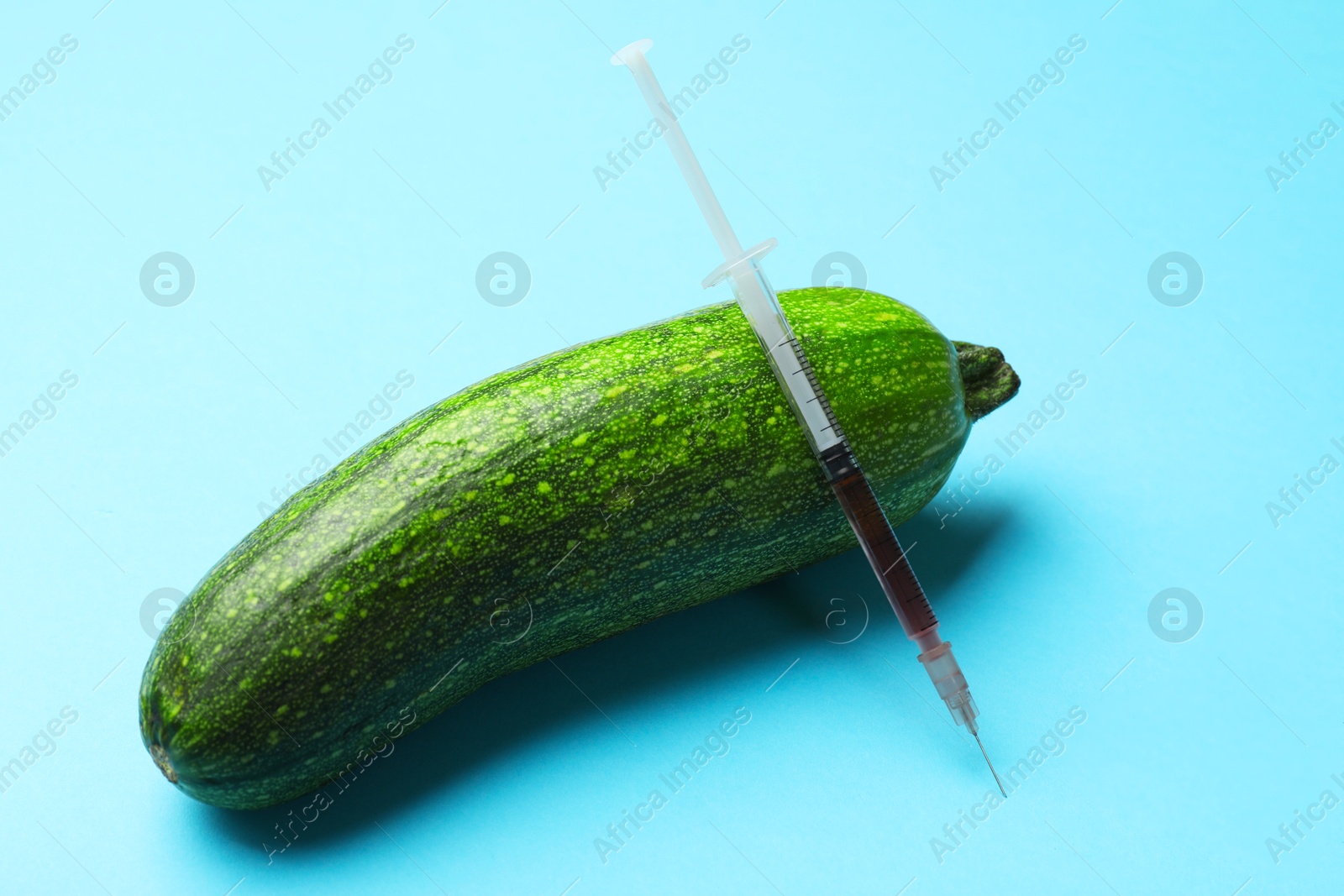 Photo of GMO concept. Zucchini and syringe with liquid on light blue background, closeup