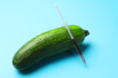 Photo of GMO concept. Zucchini and syringe with liquid on light blue background, closeup