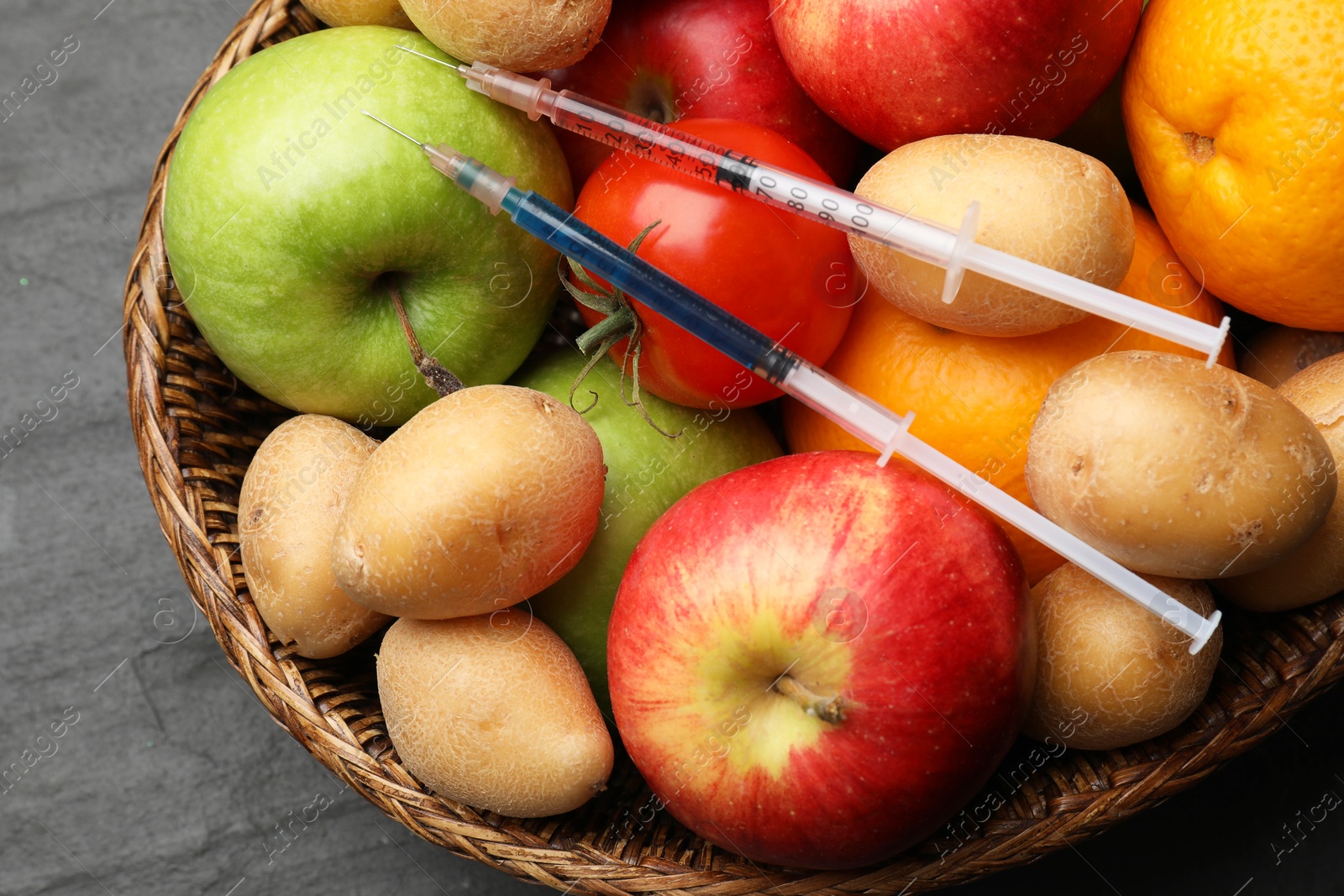 Photo of GMO concept. Different products and syringes in basket on grey textured table, top view