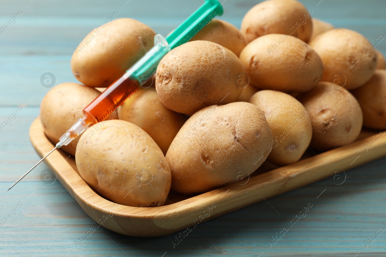 Photo of GMO concept. Potatoes and syringe with liquid on light blue wooden table, closeup