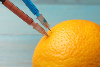 Photo of GMO concept. Orange with syringes on blurred background, closeup