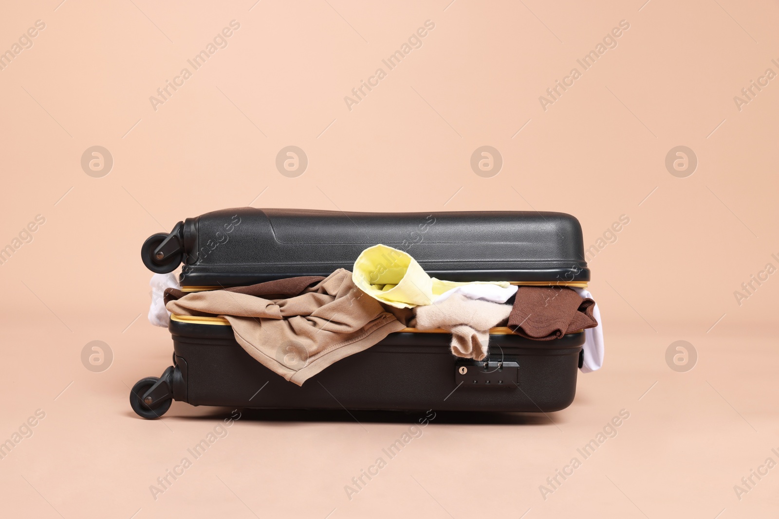 Photo of Packed suitcase full of clothes on beige background