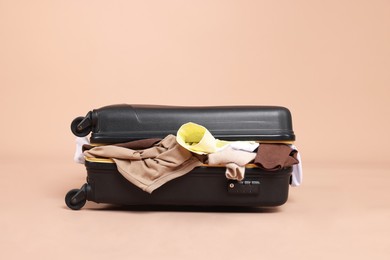 Photo of Packed suitcase full of clothes on beige background
