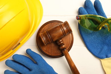 Photo of Accident at work concept. Gavel and protective gear on white wooden table, flat lay