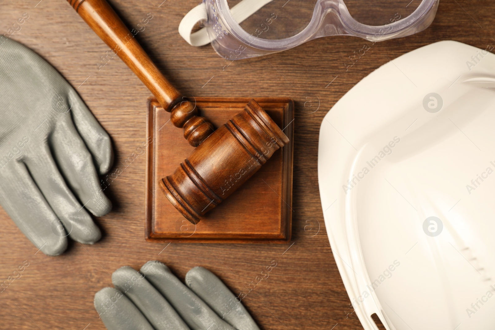 Photo of Accident at work concept. Gavel and protective gear on wooden table, flat lay