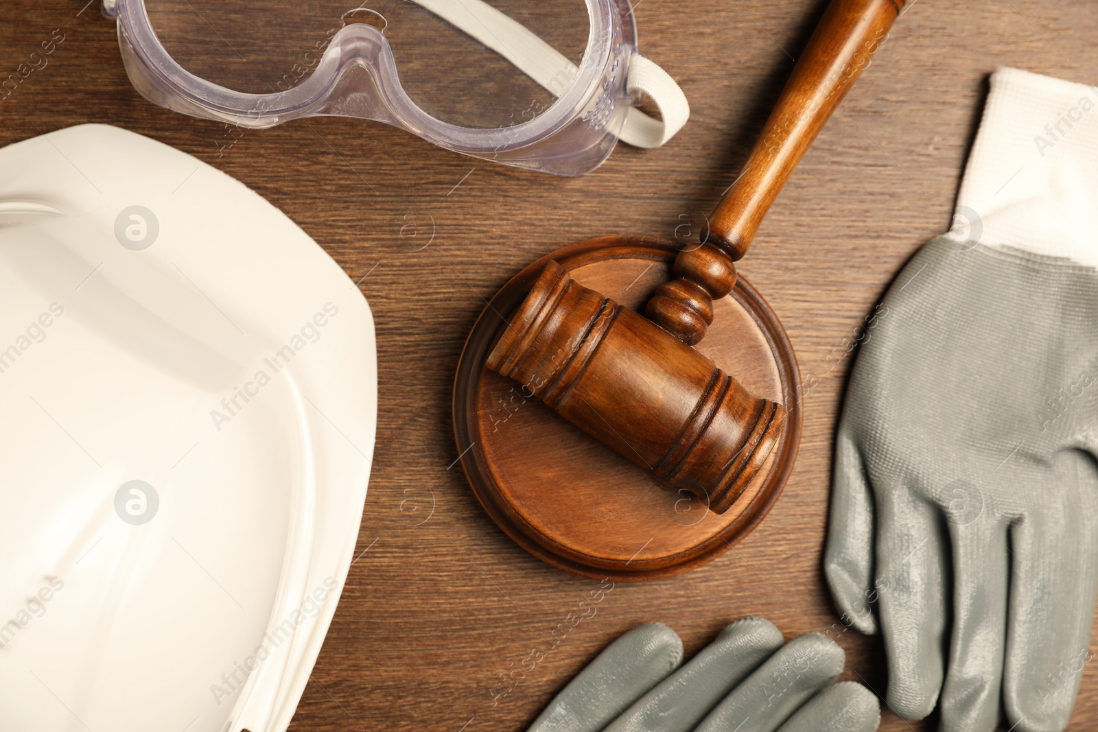 Photo of Accident at work concept. Gavel and protective gear on wooden table, flat lay