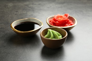 Photo of Hot wasabi paste, soy sauce and ginger on grey textured table, closeup