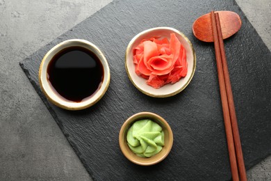 Photo of Hot wasabi paste, soy sauce, ginger and chopsticks on grey textured table, top view