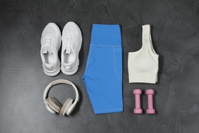 Photo of Stylish sportswear, white sneakers, dumbbells and headphones on grey background, flat lay