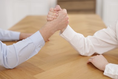 Photo of Competition concept. Businesspeople arm wrestling at table in office, closeup