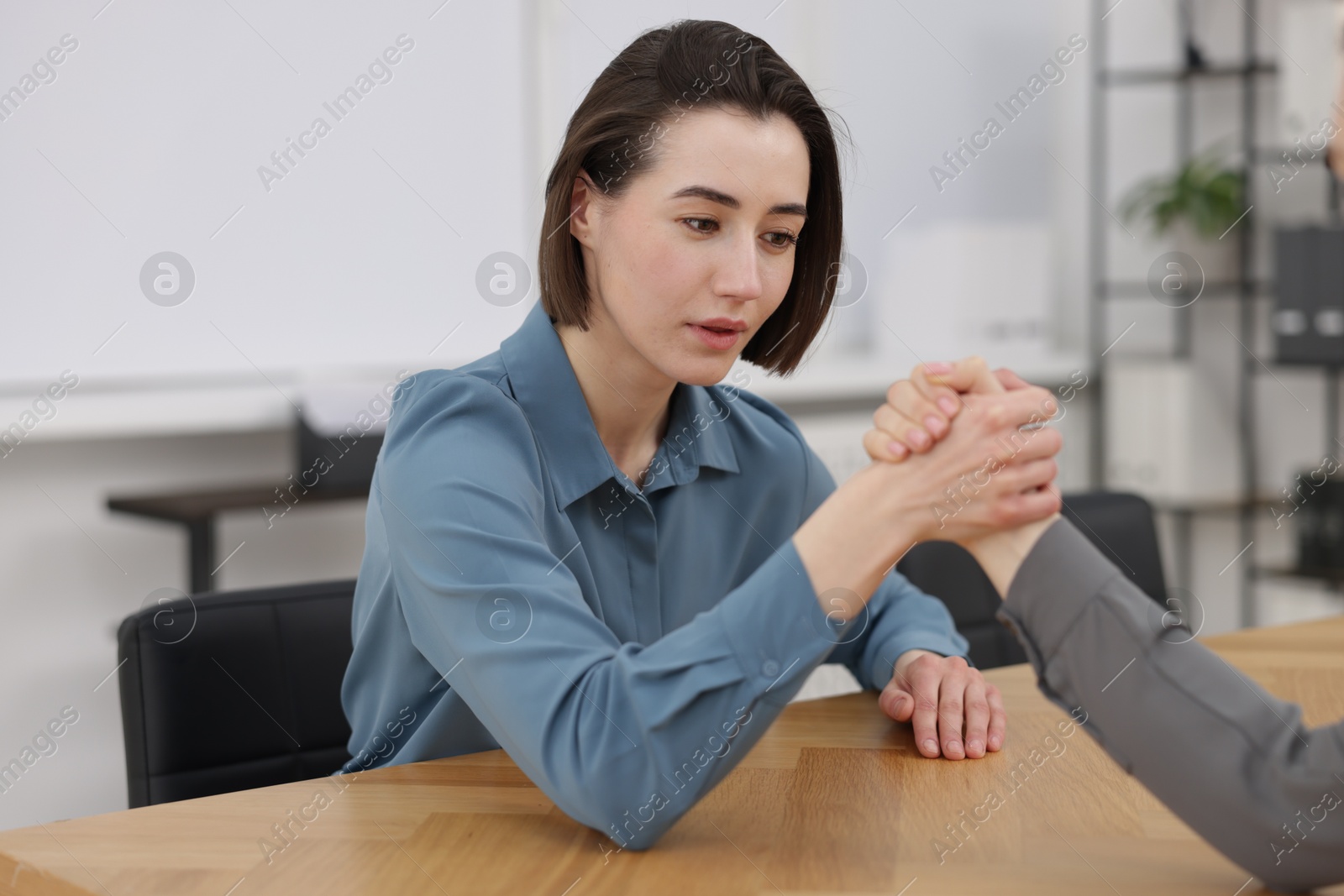 Photo of Competition concept. Businesswomen arm wrestling at table in office, closeup