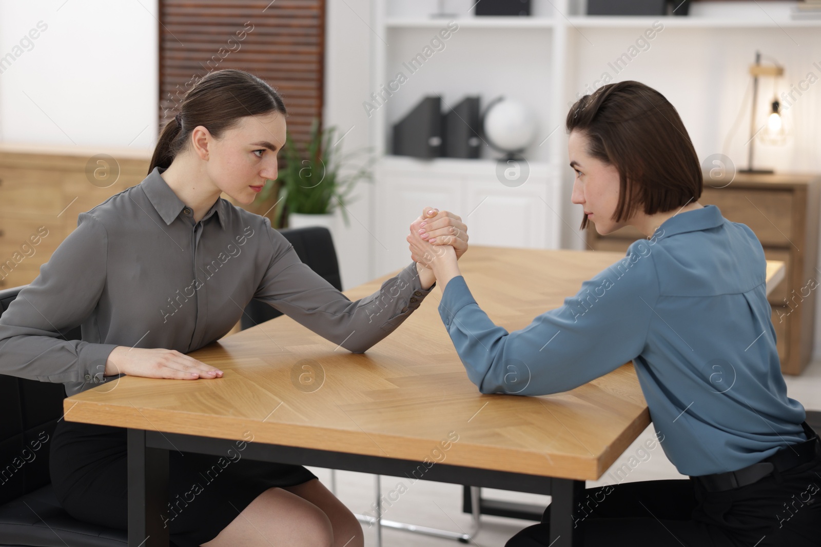 Photo of Competition concept. Businesswomen arm wrestling at table in office