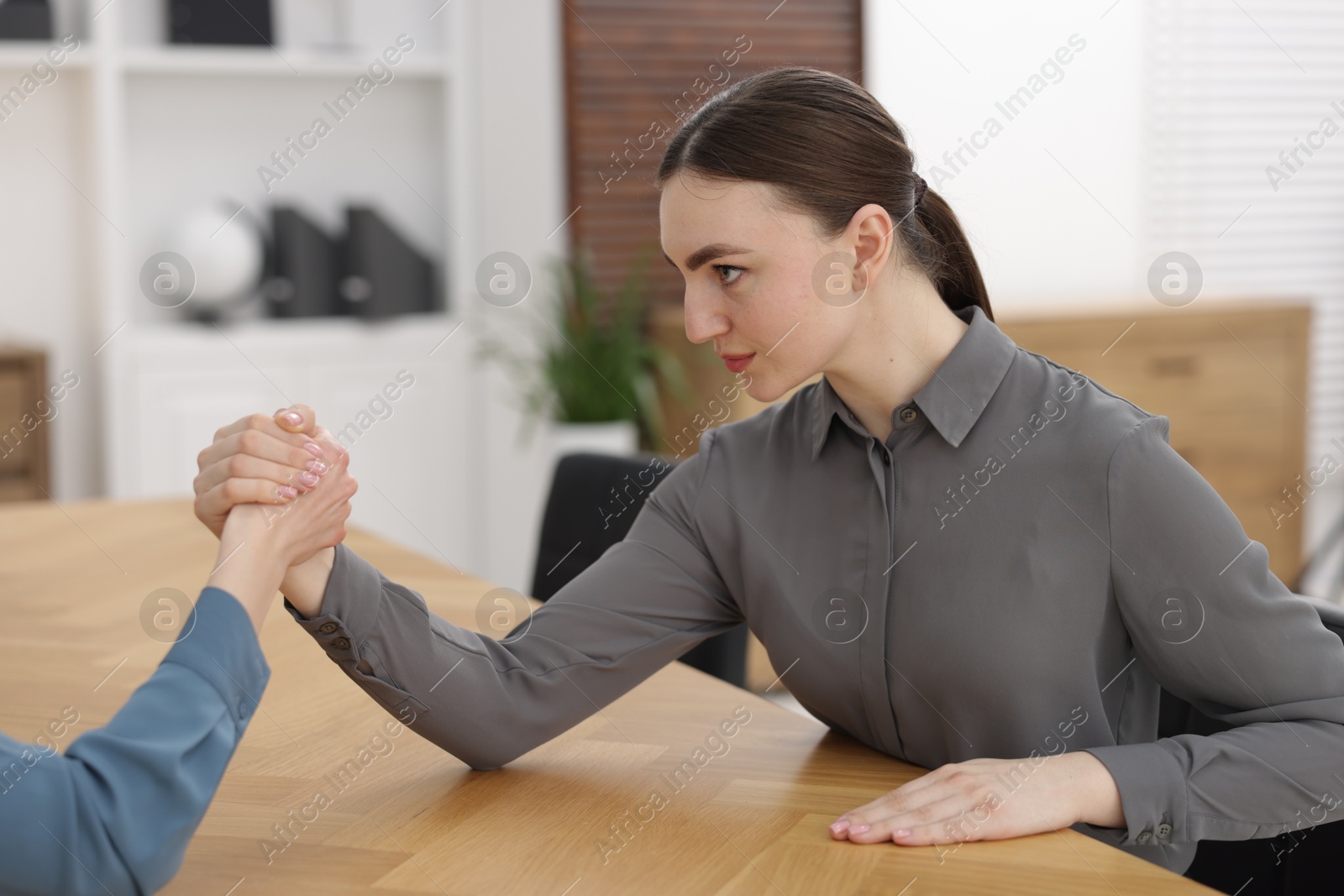 Photo of Competition concept. Businesswomen arm wrestling at table in office, closeup