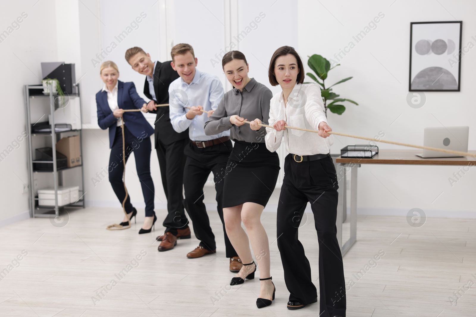 Photo of Competition concept. Group of happy businesspeople pulling rope in office