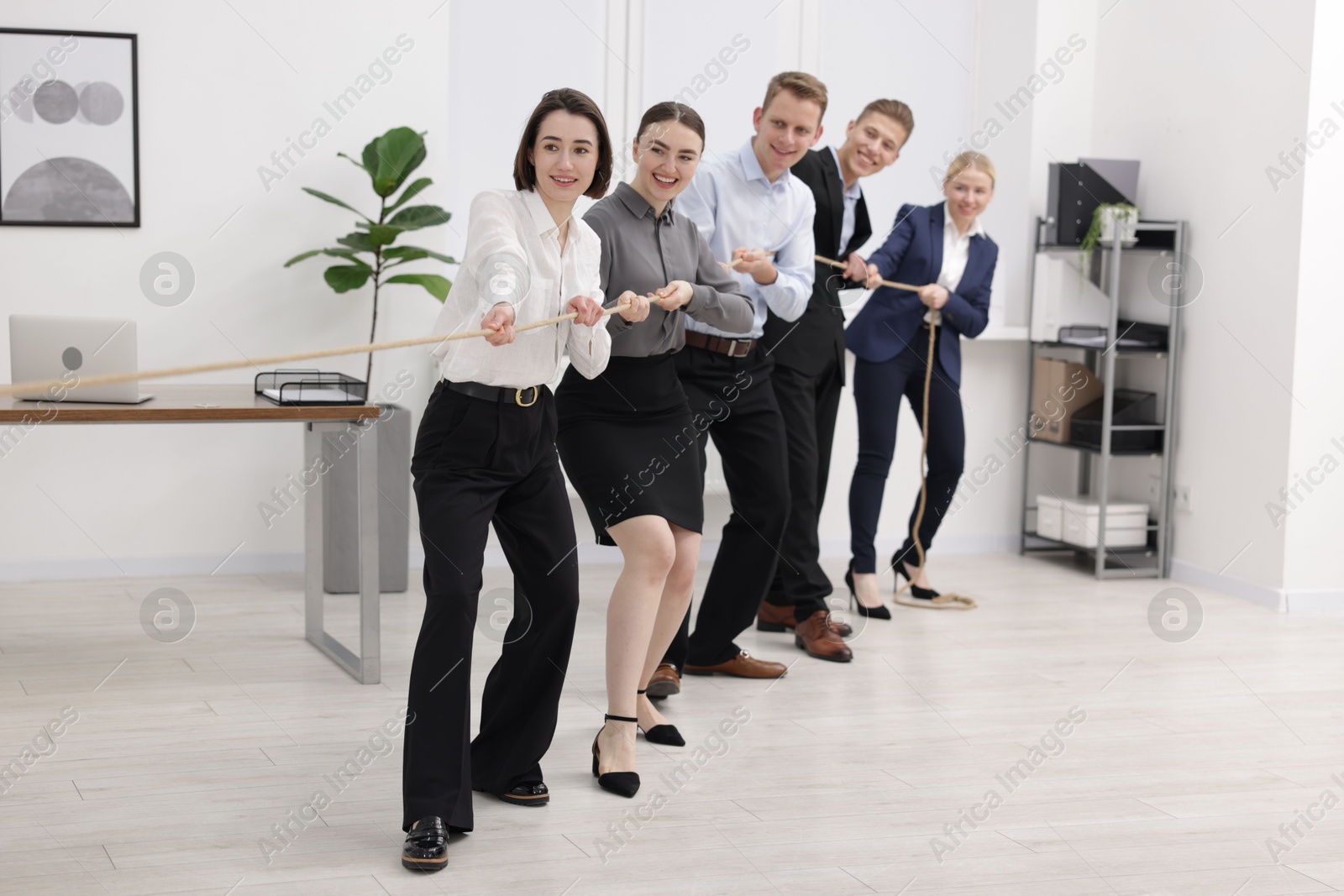 Photo of Competition concept. Group of happy businesspeople pulling rope in office