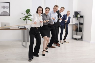 Competition concept. Group of happy businesspeople pulling rope in office