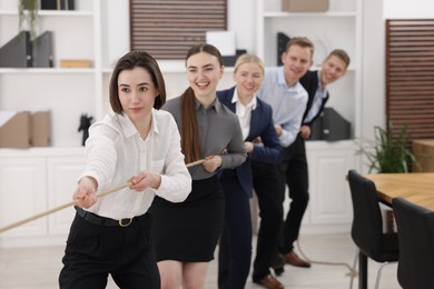 Competition concept. Group of businesspeople pulling rope in office, selective focus